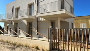 A modern two-story building with balconies, a gated entrance, and a clear sky.
