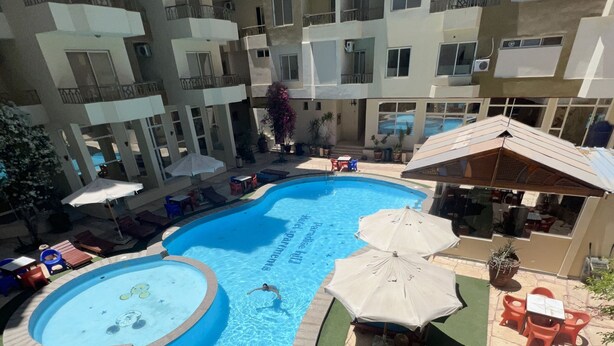 Una piscina con trampolín de clavados, rodeada de sillas de descanso y sombrillas.