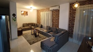 Una sala de estar moderna con un sofá modular, una mesa de centro y una alfombra. Hay una chimenea, un aire acondicionado instalado en la pared y una lámpara en el techo.