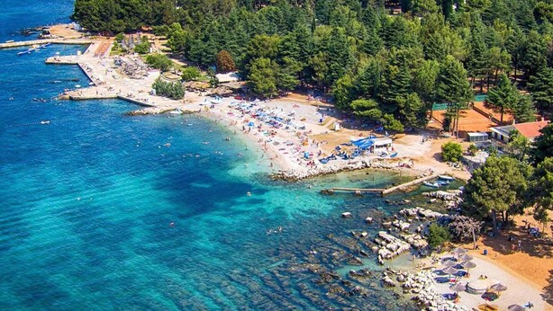 An aerial view of a coastal area with a beach, clear blue waters, and a forested hill. - Apartment Parentium - Stay in the Heart of Porec (Porec)