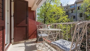 A balcony with a table and two chairs, a closed door, and a view of trees and buildings. - Apartment Parentium - Stay in the Heart of Porec (Porec)