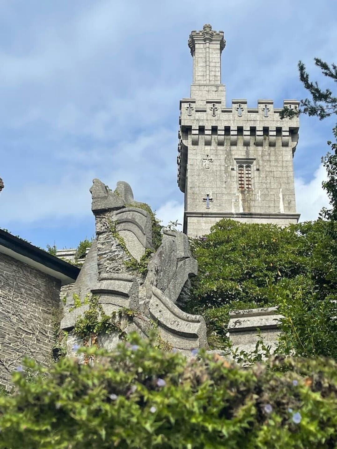 A stone tower with a cross on top, surrounded by greenery.