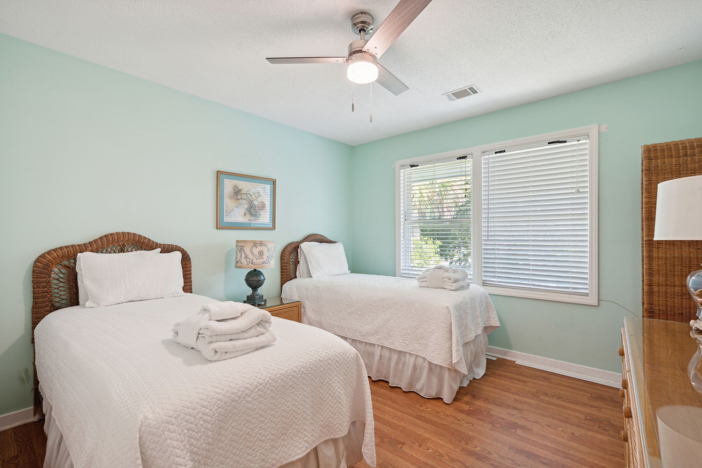 A bedroom with two beds, a ceiling fan, and a window with blinds.