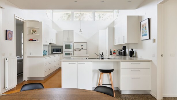 Une cuisine moderne avec des meubles blancs, un îlot central et un coin repas comprenant une table en bois et des chaises noires.