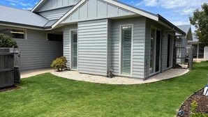 Une maison d’habitation avec un revêtement extérieur gris, un petit jardin à l’avant avec une pelouse bien entretenue et une clôture en bois.