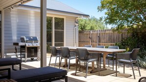 Une terrasse avec un barbecue, une table à manger et des chaises.