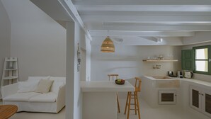 A modern kitchen with white cabinetry, a wooden island with stools, and a hanging light fixture. - Two-bedroom Family Cave Suite with private terrace, kitchenette | Element Suites (Thira - Santorini)