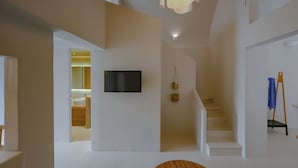 A modern interior with a staircase, a flat-screen TV mounted on the wall, and a wooden bench with a blue towel. - Two-bedroom Family Cave Suite with private terrace, kitchenette | Element Suites (Thira - Santorini)