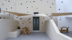 A modern interior with a minimalist design, featuring a wooden table and chairs, a small potted plant, and a door with a green frame. - Deluxe Cave Suite with large private terrace & kitchenette | Element Suites (Thira - Santorini)