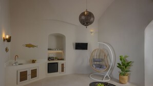 A modern kitchen with a built-in dishwasher, a hanging chair, a small dining table, and a potted plant. - Deluxe Cave Suite with large private terrace & kitchenette | Element Suites (Thira - Santorini)