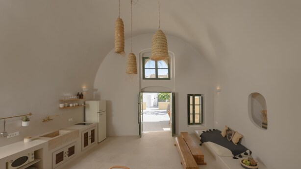 A modern kitchen with a central island, wooden benches, and a view to the dining area.