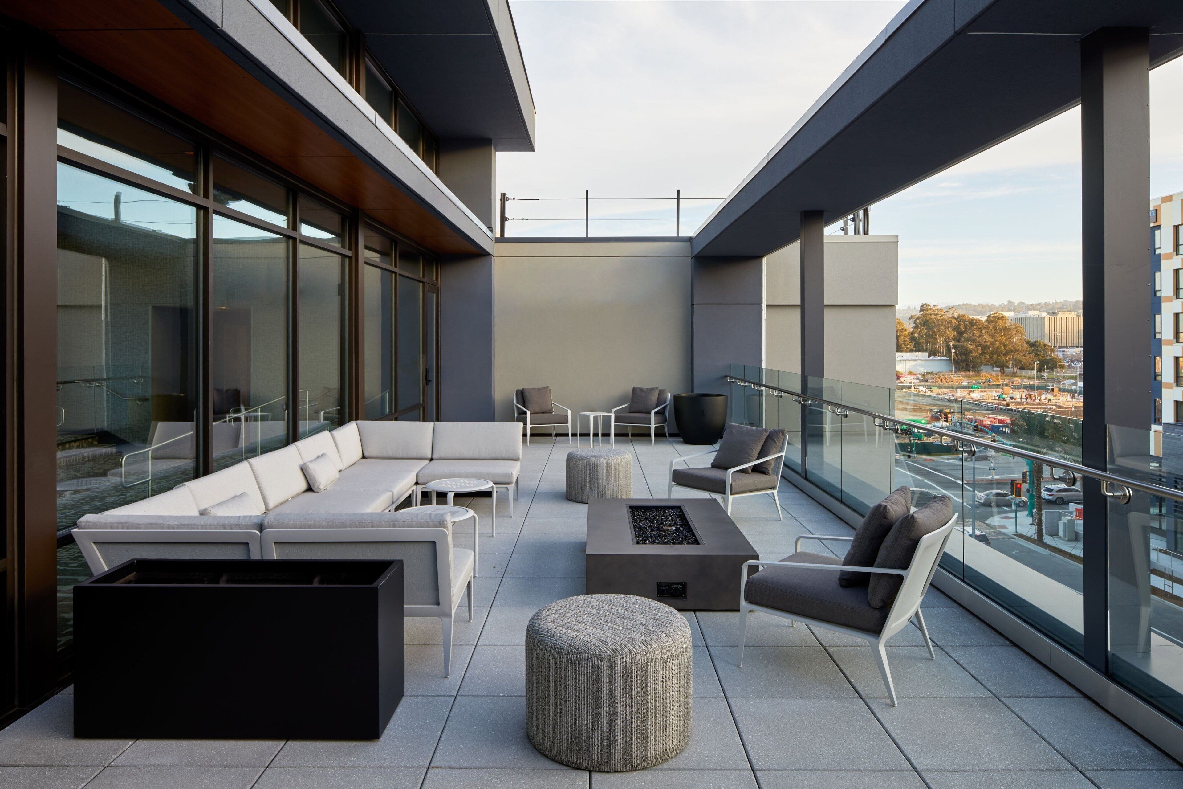 Un espacio lounge moderno al aire libre con un conjunto de sofás, otomanas y un hogar para fuego.
