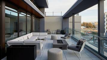 Un espacio lounge moderno al aire libre con un conjunto de sofás, otomanas y un hogar para fuego.