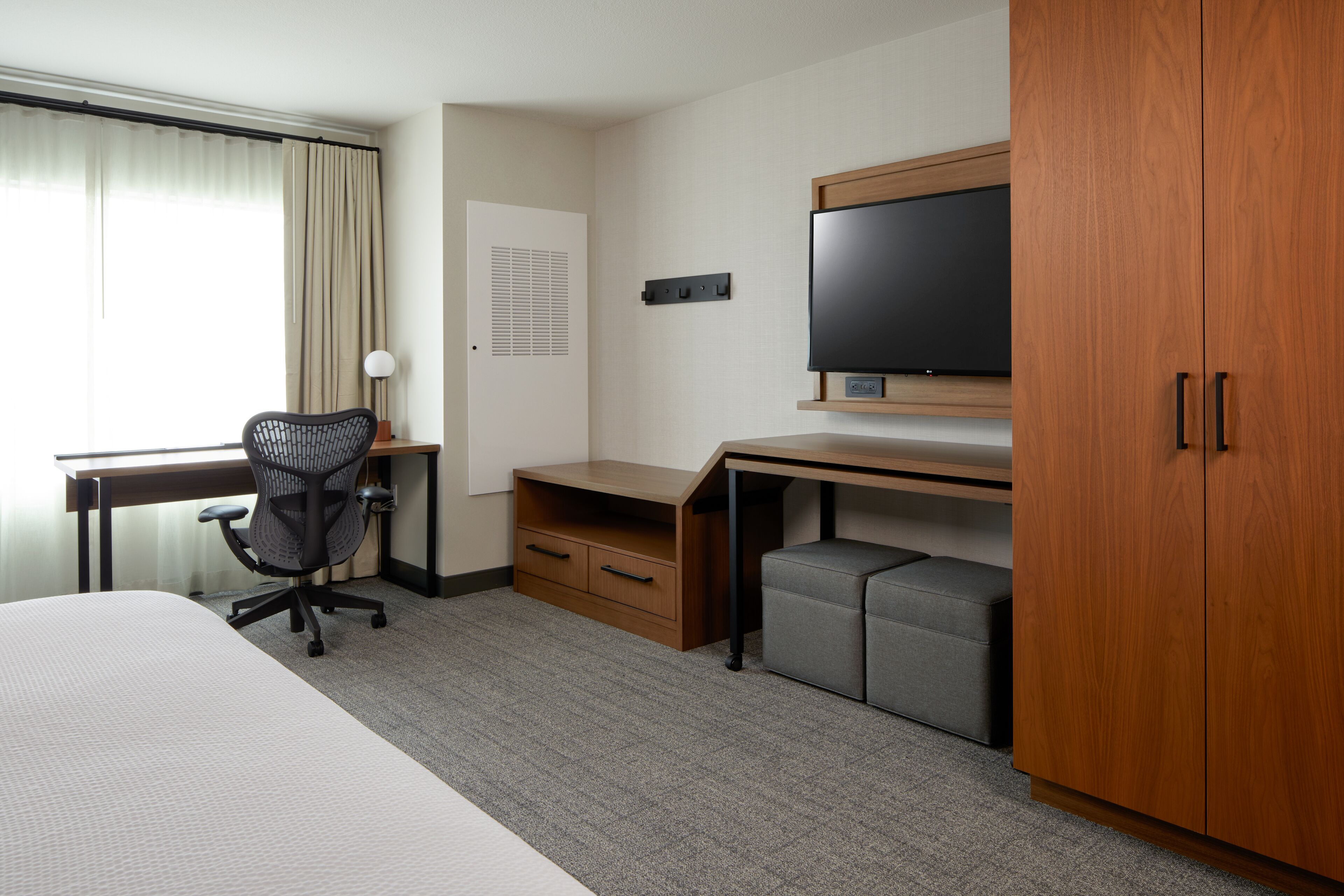 Hotelkamer met een bed, bureau, stoel, televisie, kledingkast en raam met gordijnen.