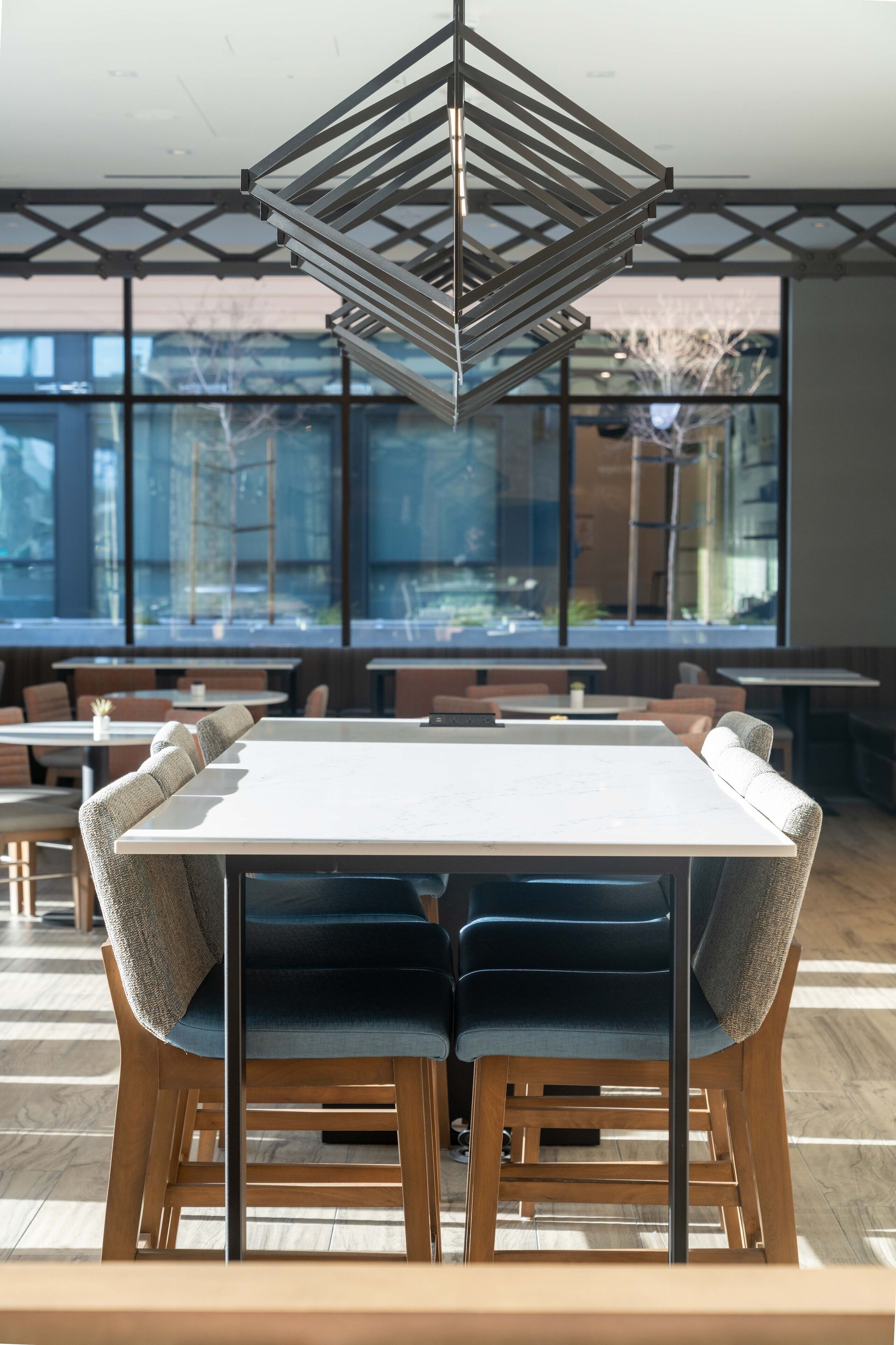 A modern dining area with a central table, cushioned chairs, and a geometric pendant light.
