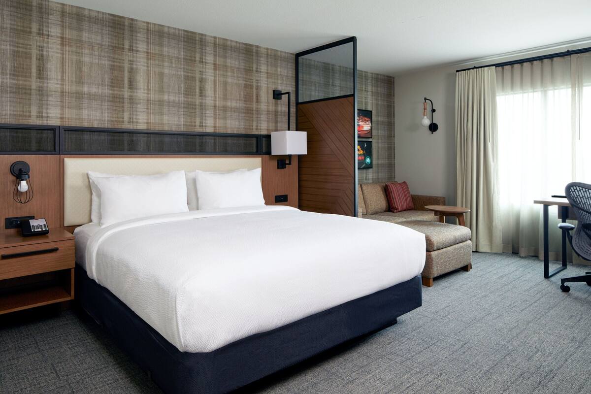 A hotel room with a large bed, a desk, a chair, and a sofa.
