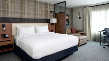 A hotel room with a large bed, a desk, a chair, and a sofa.