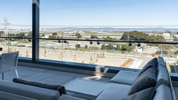 A modern hotel room with a large window offering a view of an airport and distant mountains.