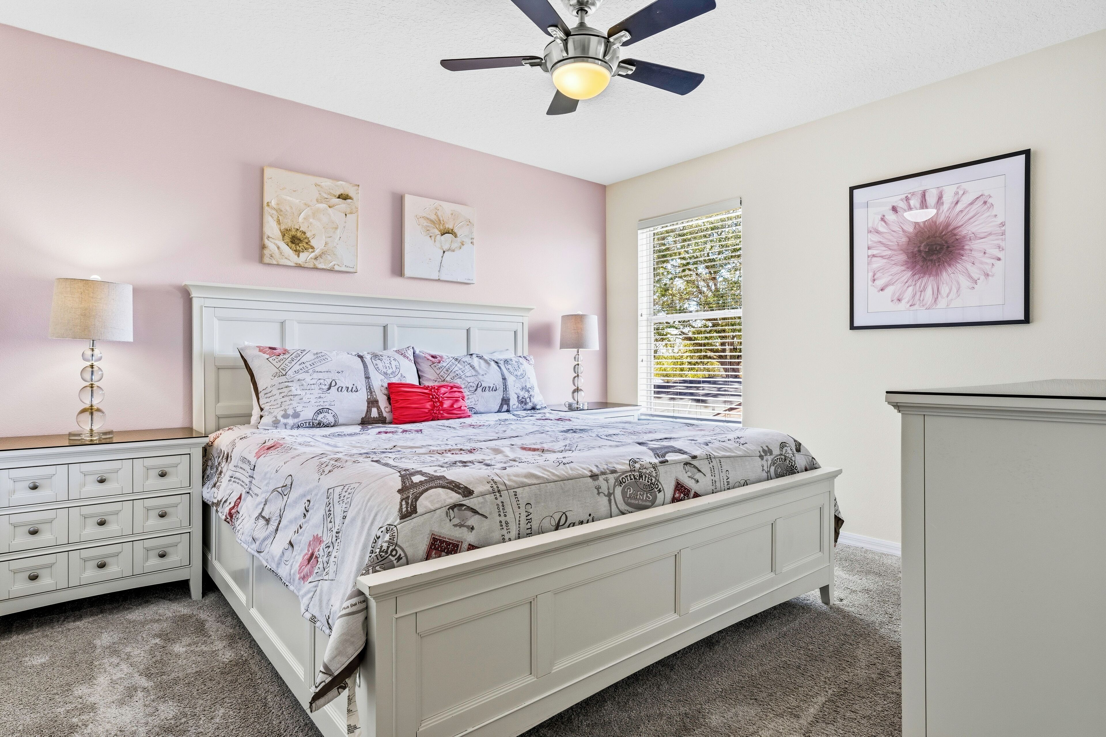A bedroom with a bed, bedside tables, a ceiling fan, and artwork on the walls.