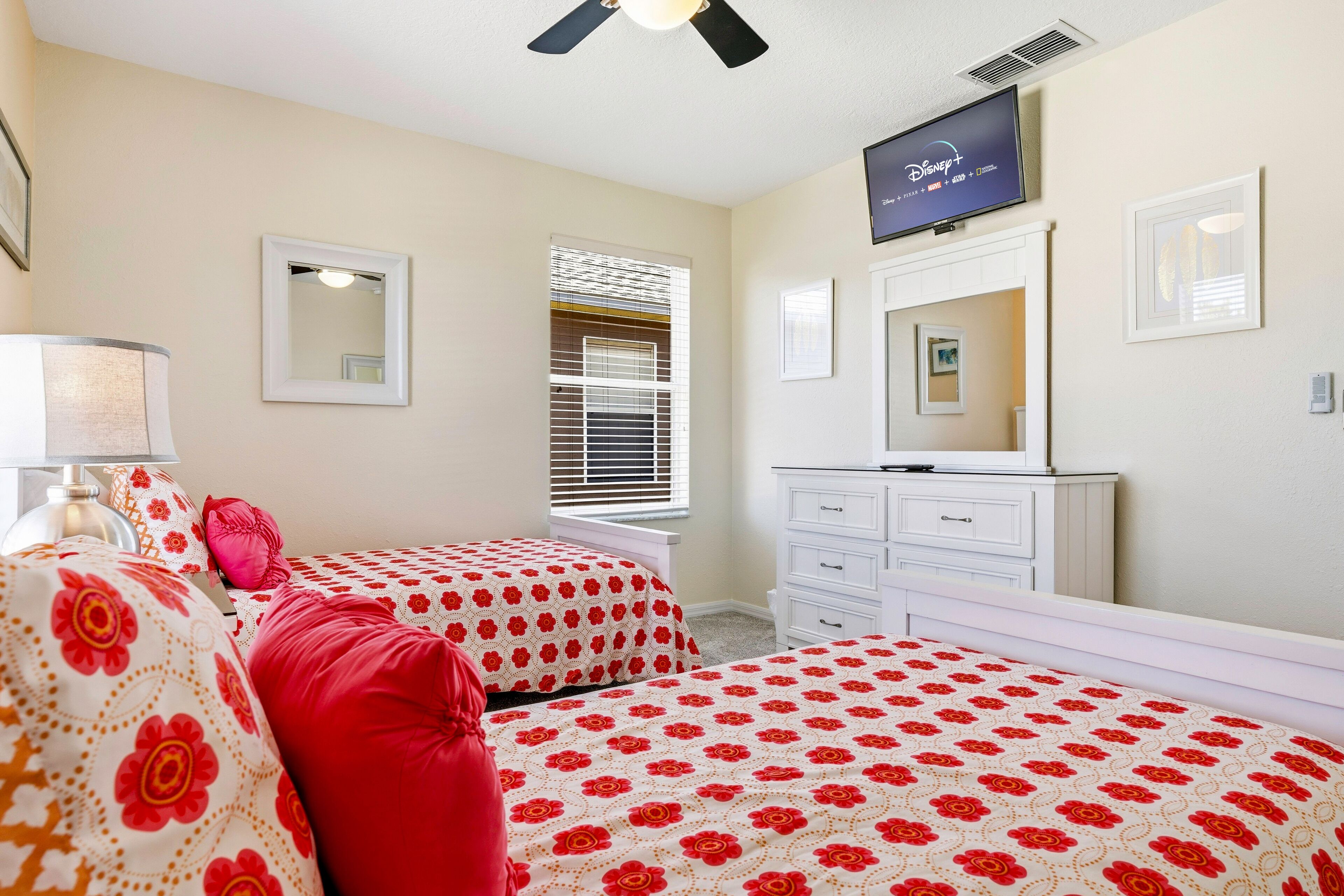 A bedroom with two beds, a TV, a dresser, and a window with blinds.