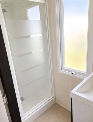 A bathroom with a glass shower door, a window, and a white sink. - Location de Mobil Home Camping Tohapi en Alsace (Biesheim)