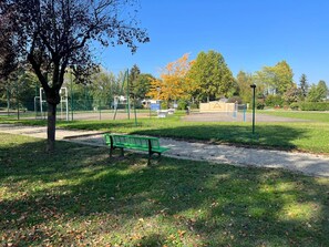 A park with a green bench, a soccer field, and a playground. - Location de Mobil Home Camping Tohapi en Alsace (Biesheim)