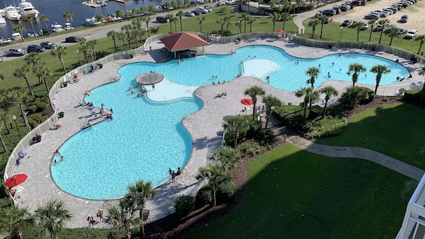 A large, multi-pond swimming area with a surrounding deck, palm trees, and a marina in the background. - Yacht Club Villas #2-405 Extraordinary and Spacious Condo! (North Myrtle Beach)