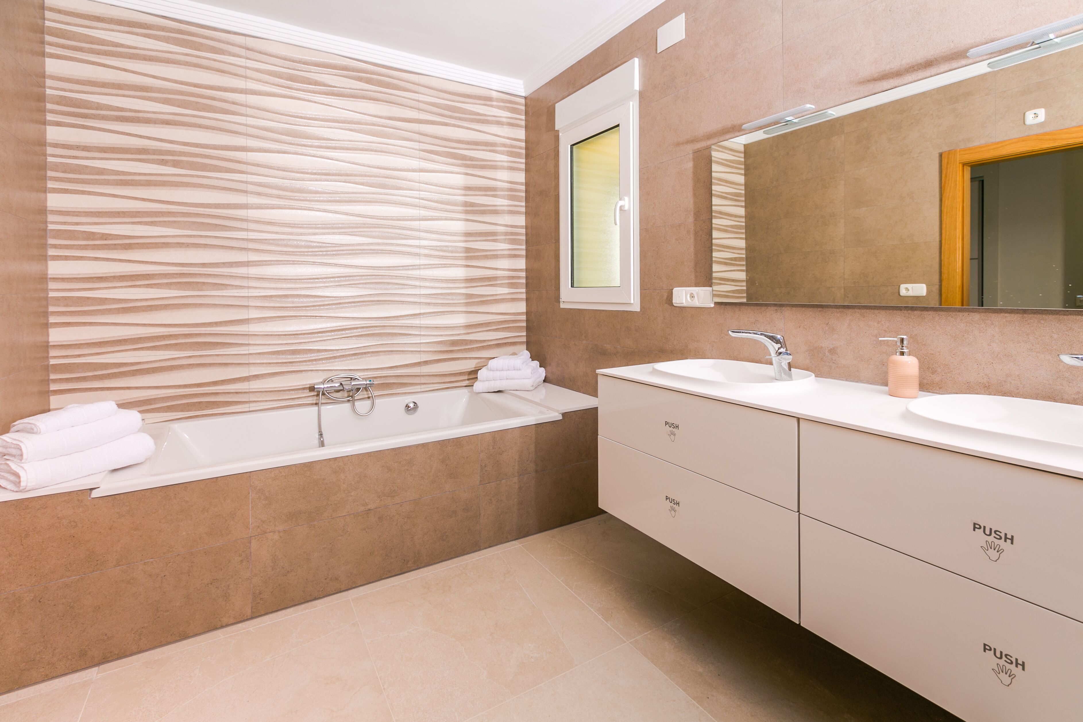 A modern bathroom with a bathtub, two sinks, and a large mirror.