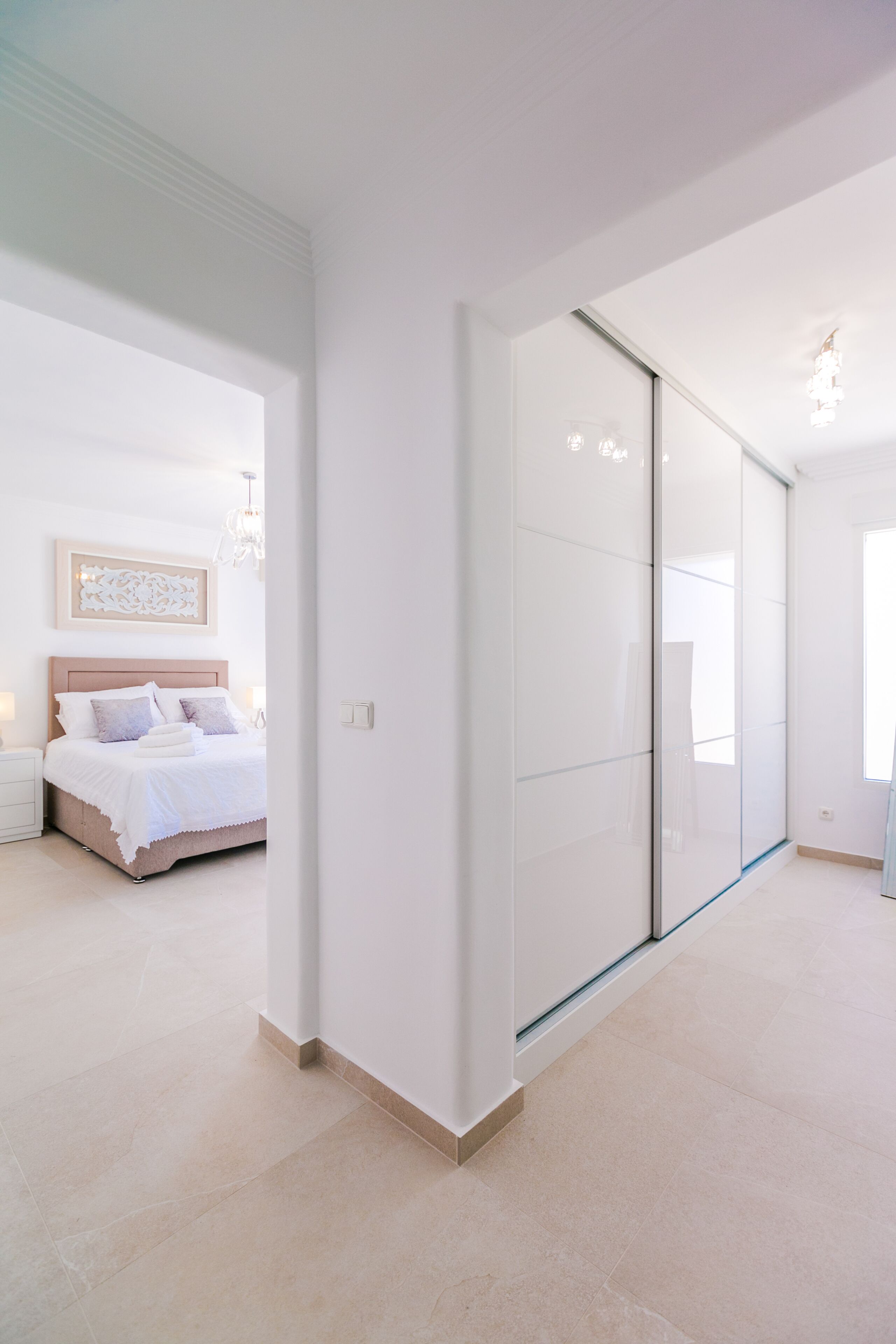Ein modernes Schlafzimmer mit einem großen Bett, einer Glastrennwand und einer Chandelier.