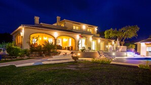 A large, well-lit house with a swimming pool, outdoor seating, and a landscaped garden.