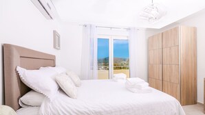 A bedroom with a large bed, a wardrobe, and a balcony with a view.