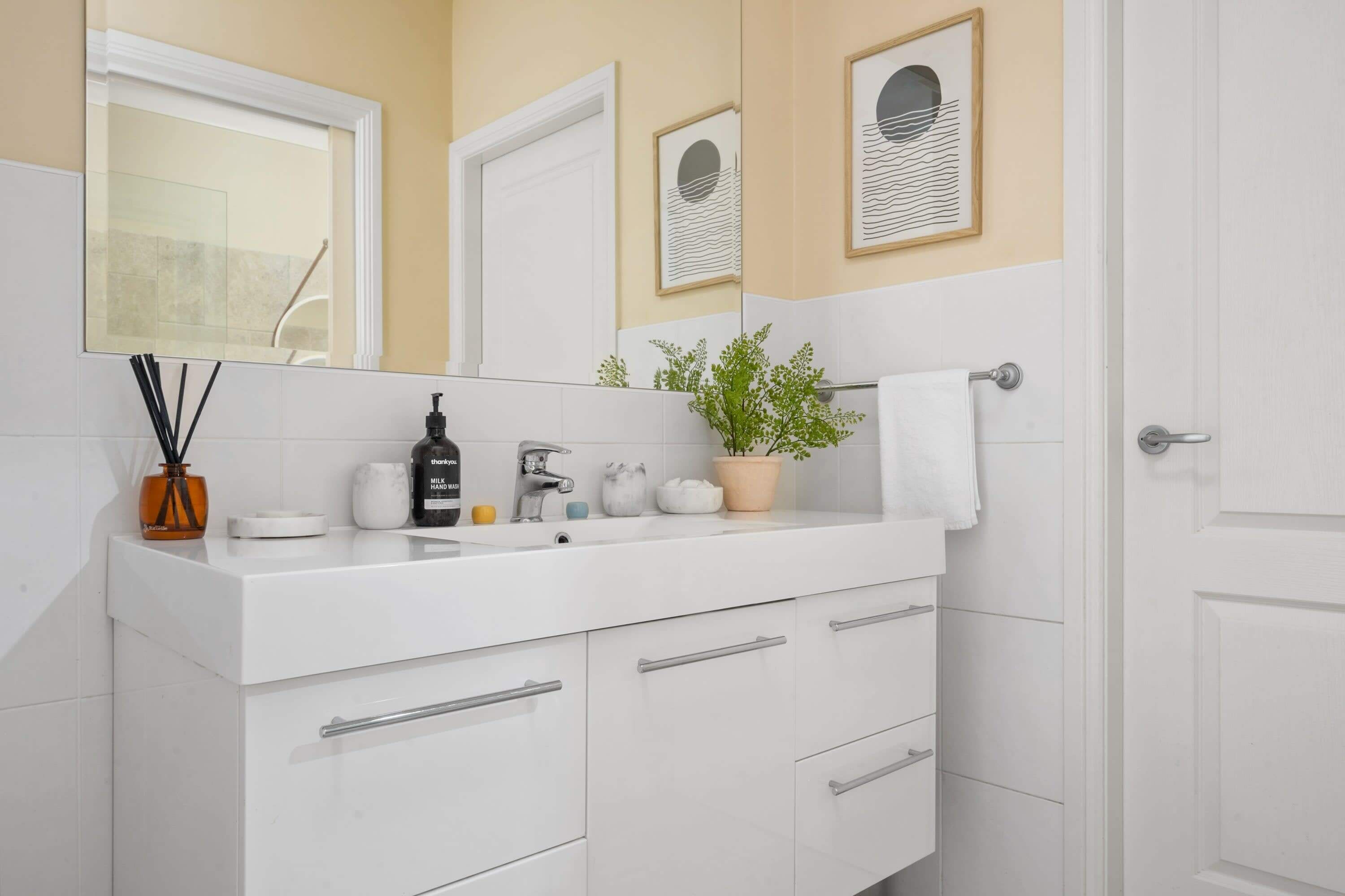 Een moderne badkamer met een wit wastafelmeubel, een grote spiegel en een potplant.