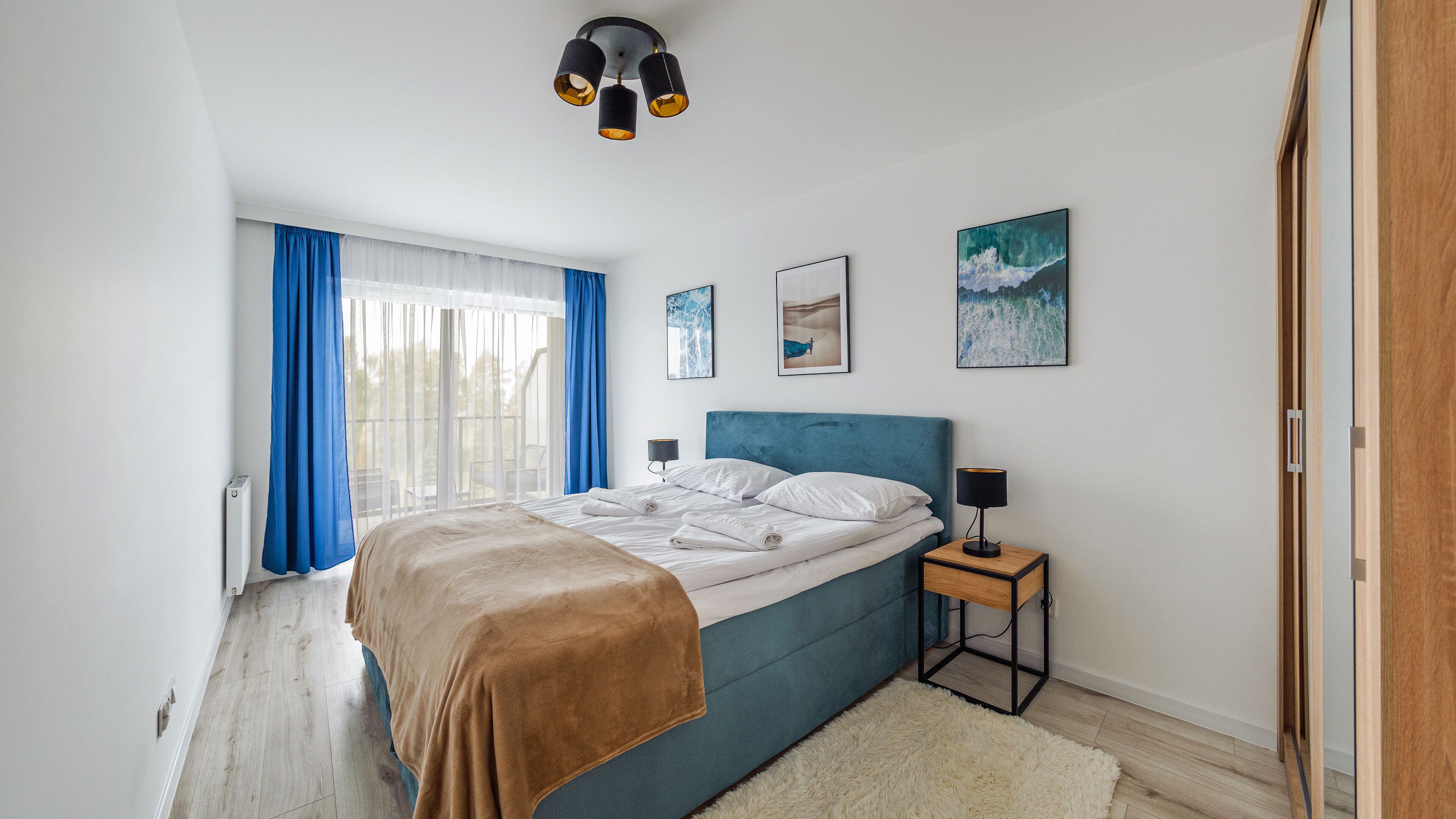 A bedroom with a bed, a bedside table, a lamp, and artwork on the wall.