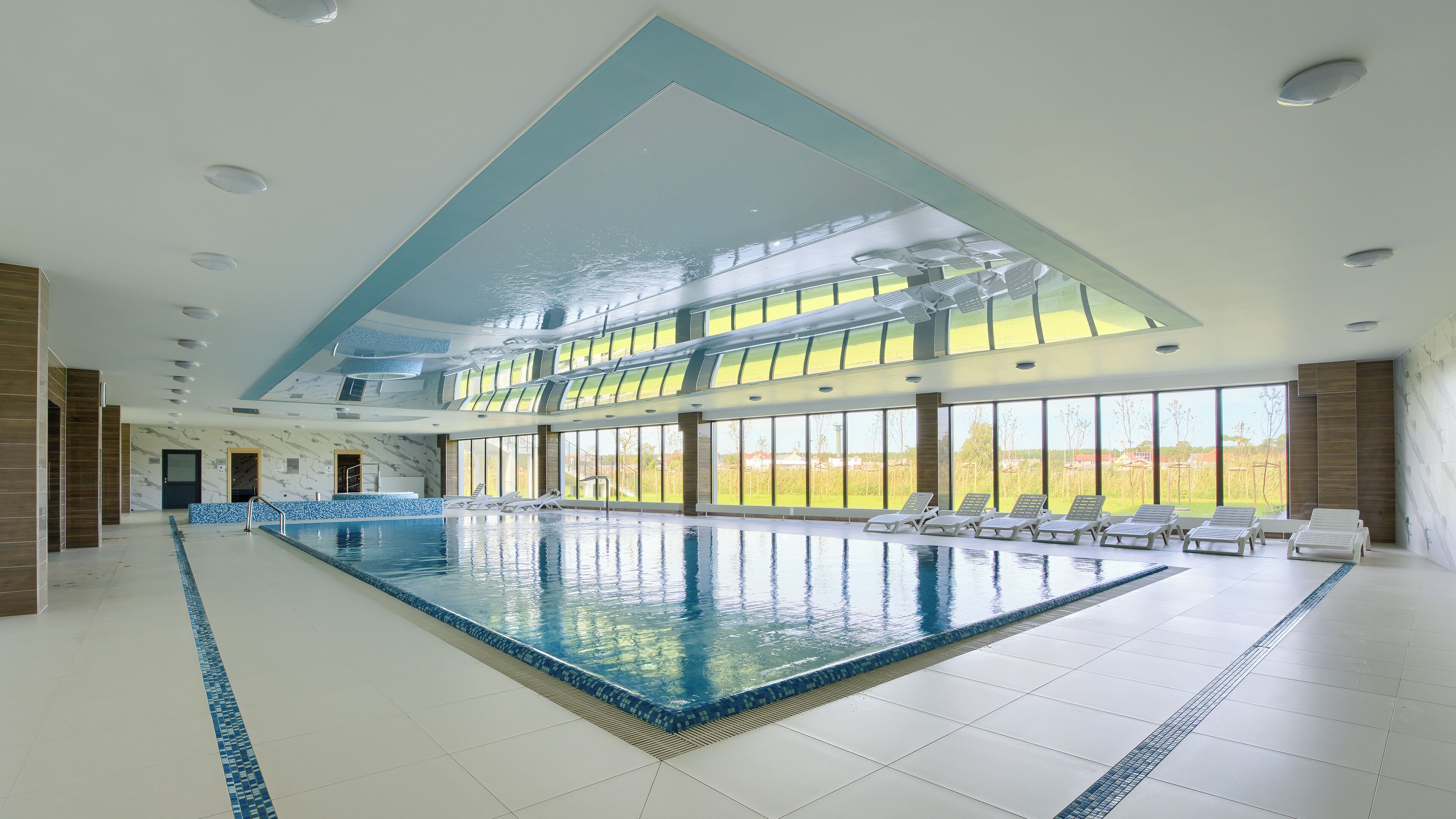 Ein Innenpool mit großen Glaswänden, einem sonnendurchfluteten Sitzbereich und Blick ins Freie.