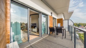 Un balcón con puerta de cristal que da a una habitación, una mesa con sillas y vistas de los alrededores.