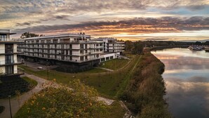 Un edificio moderno de varios pisos con techo plano, situado junto a un río tranquilo.