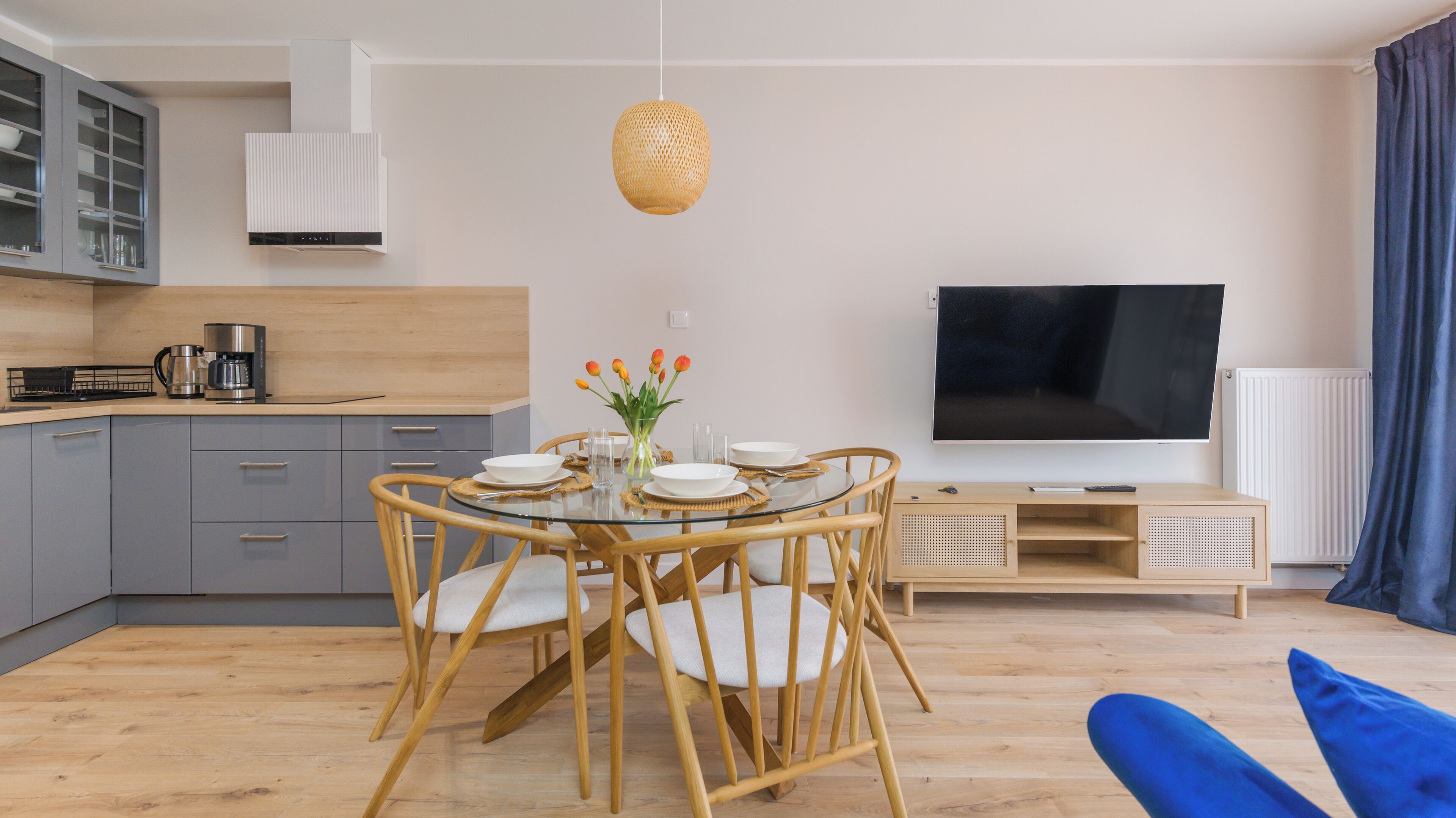 Una cucina moderna con mobili grigi, una macchina per il caffè e un'area pranzo con tavolo in vetro e sedie in vimini.