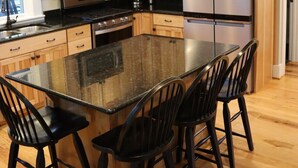 A modern kitchen with wooden cabinets, a stainless steel refrigerator, a microwave, and a large island with bar stools.