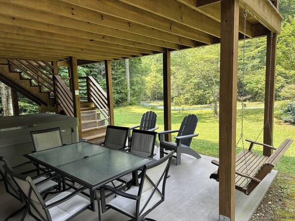 An outdoor covered patio with a table and chairs, a swing, and a view of a forested area.