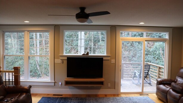 A living room with a fireplace, a ceiling fan, and large windows.