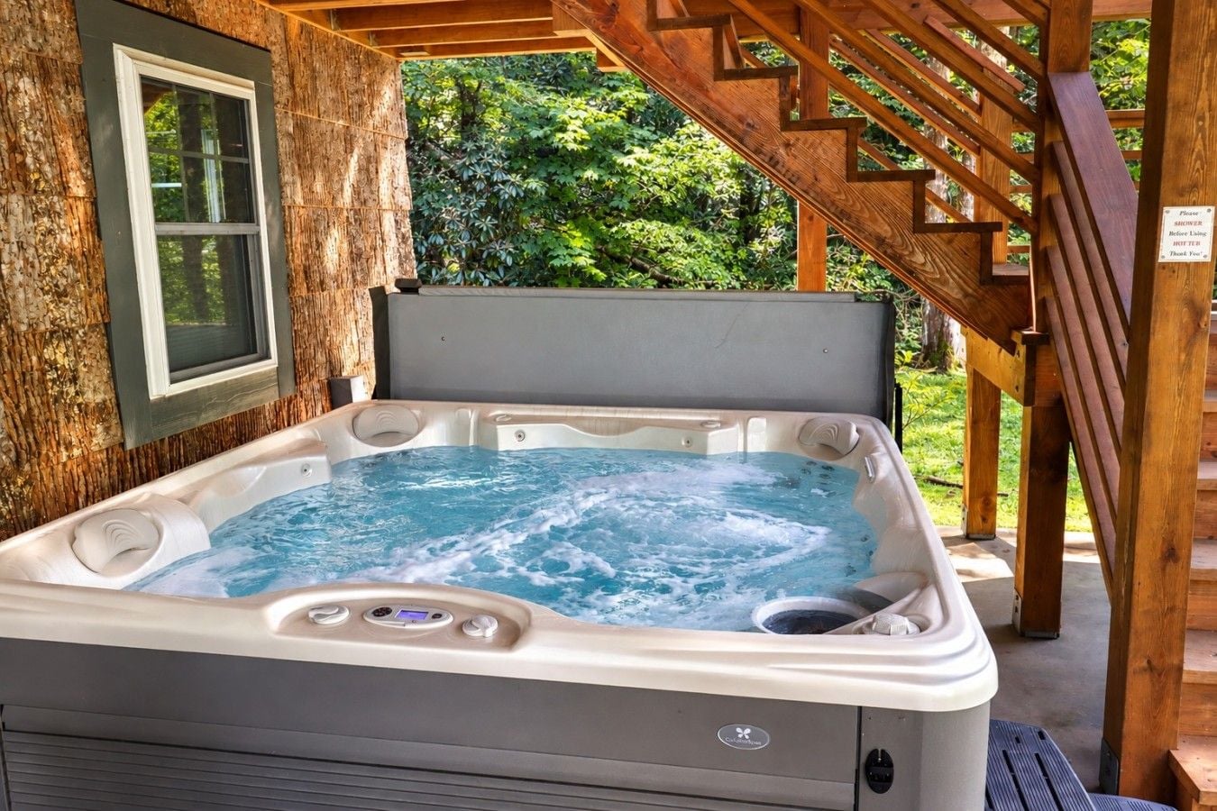 A hot tub with a wooden deck and a staircase leading to a covered area.