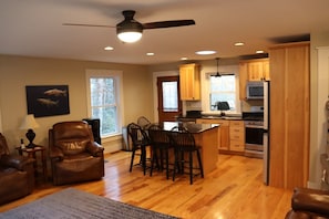 A spacious living room with a leather sofa, a dining area with chairs, a kitchen with wooden cabinets and appliances, and a ceiling fan. - Private, River, Hot tub, Fire table, fishing (Marion)