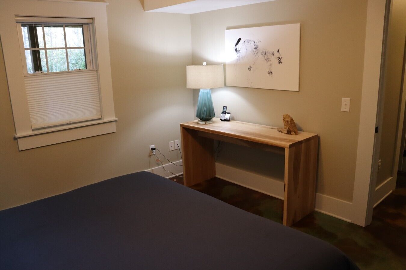Ein Schlafzimmer mit einem Bett, einem Schreibtisch, einer Lampe und einem Bild an der Wand.