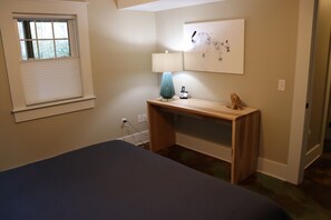 A bedroom with a bed, a desk, a lamp, and a painting on the wall.