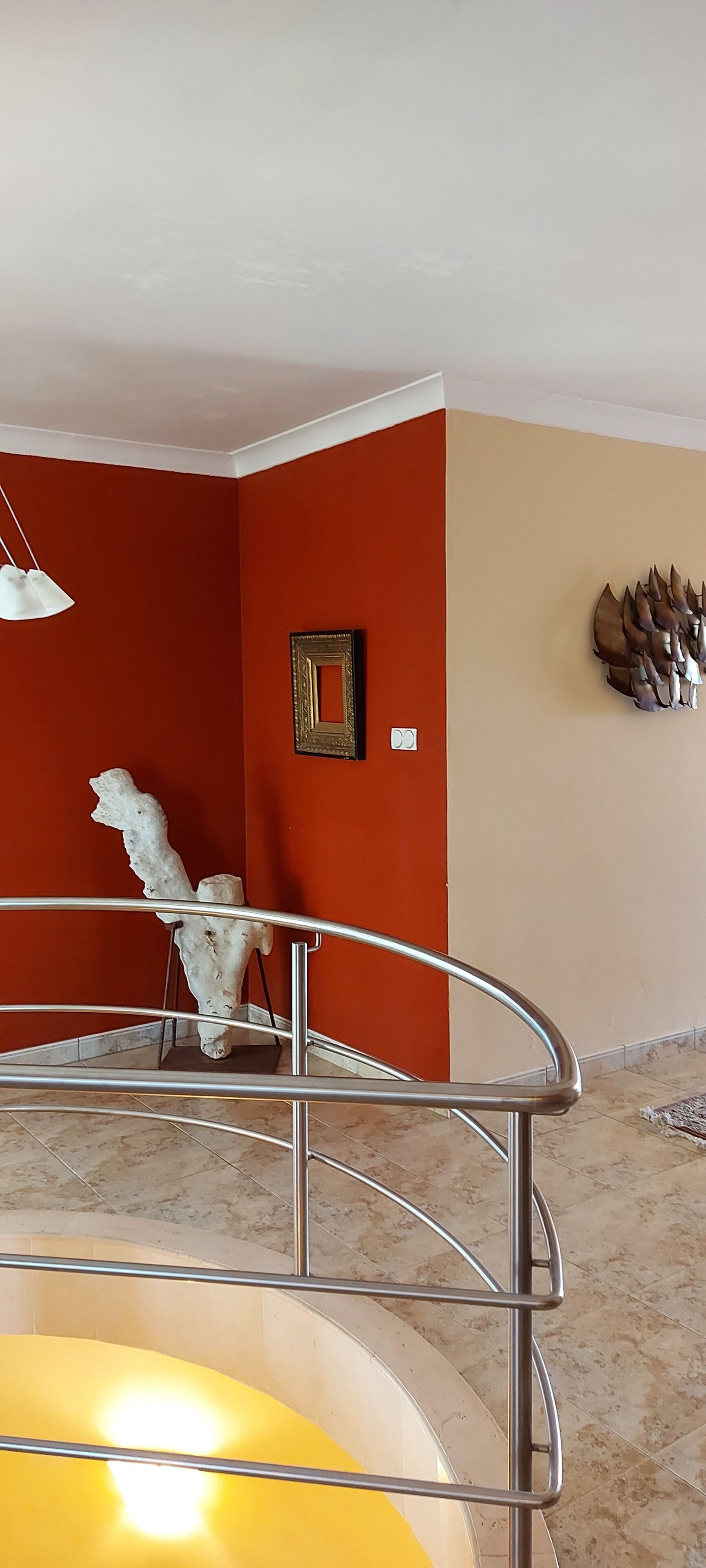 A room with a red and beige wall, a white abstract sculpture, a framed picture, and a metal railing.