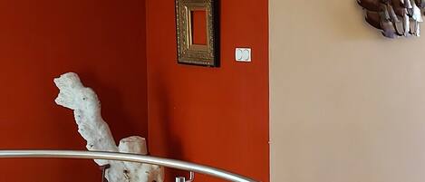 A room with a red and beige wall, a white abstract sculpture, a framed picture, and a metal railing.