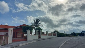 Un lotissement résidentiel fermé, avec une maison au toit rouge, un palmier et un ciel nuageux.