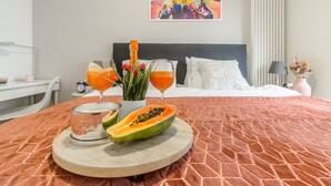 A neatly made bed with a pink textured bedspread, a wooden tray with a half-cut papaya, two glasses of orange juice, and a vase with red flowers. - Lumina cozy apartament in Warsaw (Warsaw)