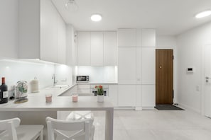 A modern kitchen with white cabinetry, a dining table with chairs, a microwave, and a wooden door. - Lumina cozy apartament in Warsaw (Warsaw)