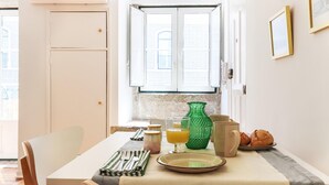 Un coin repas avec une table dressée pour deux personnes, un vase vert, une assiette et un verre de jus d’orange.